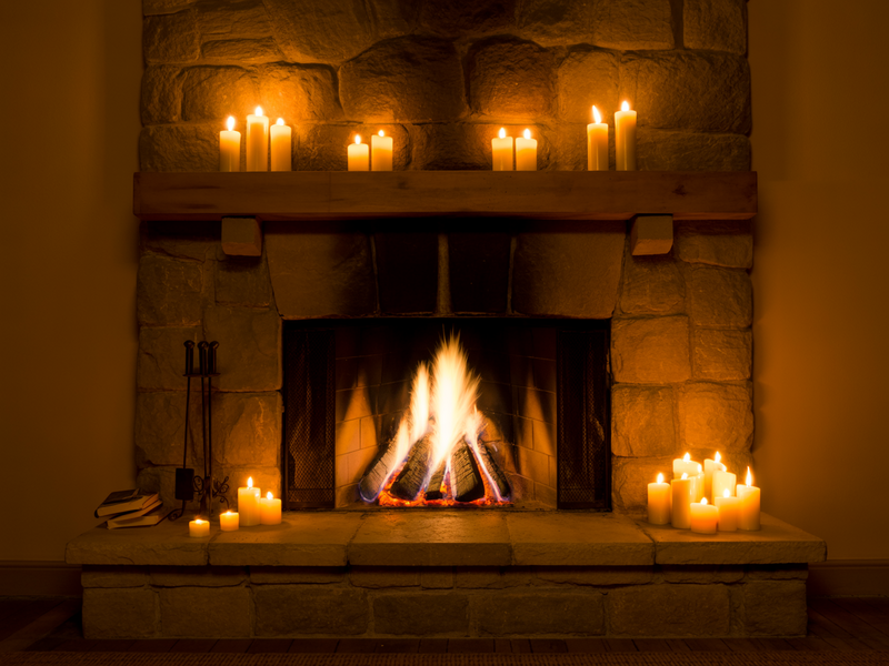 A stone fireplace with a roaring fire and candles, the warmth that inspired The Writer's Hearth